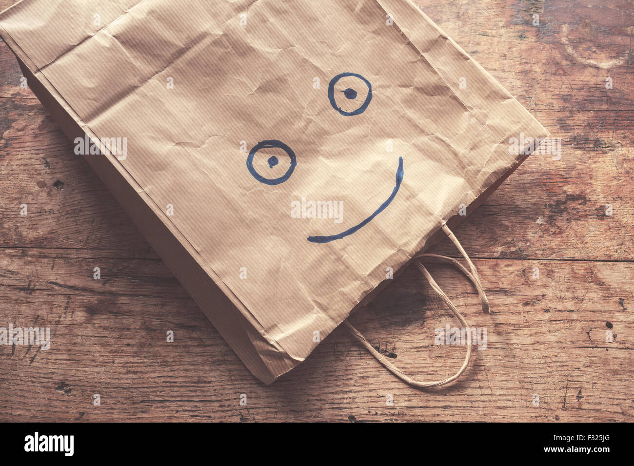 Eine Papiertüte mit einem lächelnden Gesicht gemalt auf einem Holztisch liegend Stockfoto