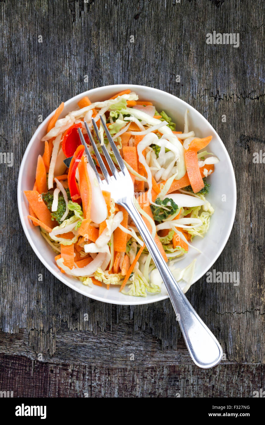 Schüssel mit Salat und Gabel auf einem groben hölzernen Hintergrund Stockfoto