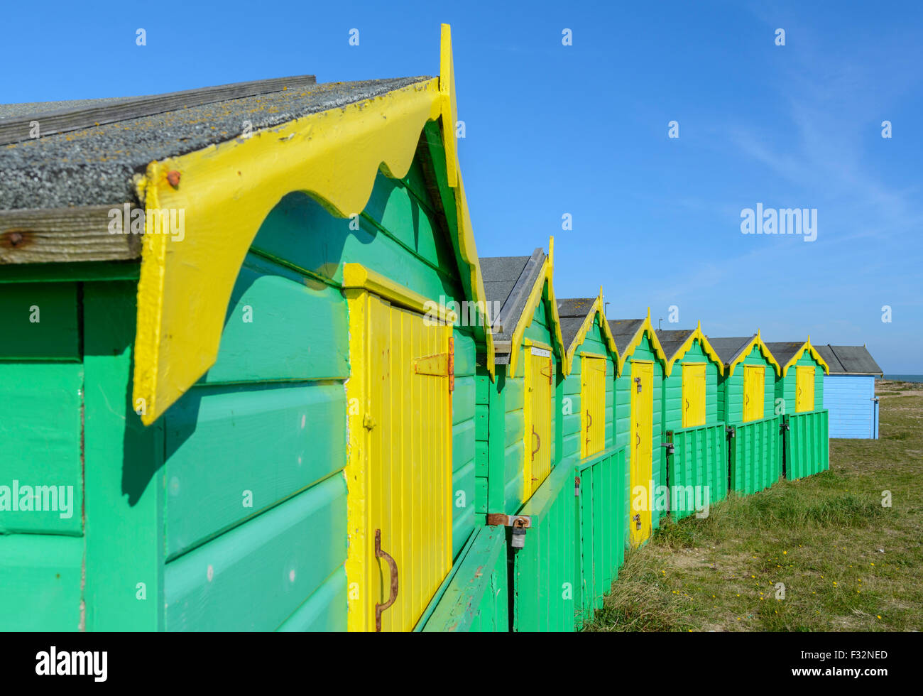 Badehäuschen UK. Reihe von grünen und gelben Strand Hütten an einem sonnigen Tag mit blauem Himmel in Littlehampton, West Sussex, England, UK. Stockfoto