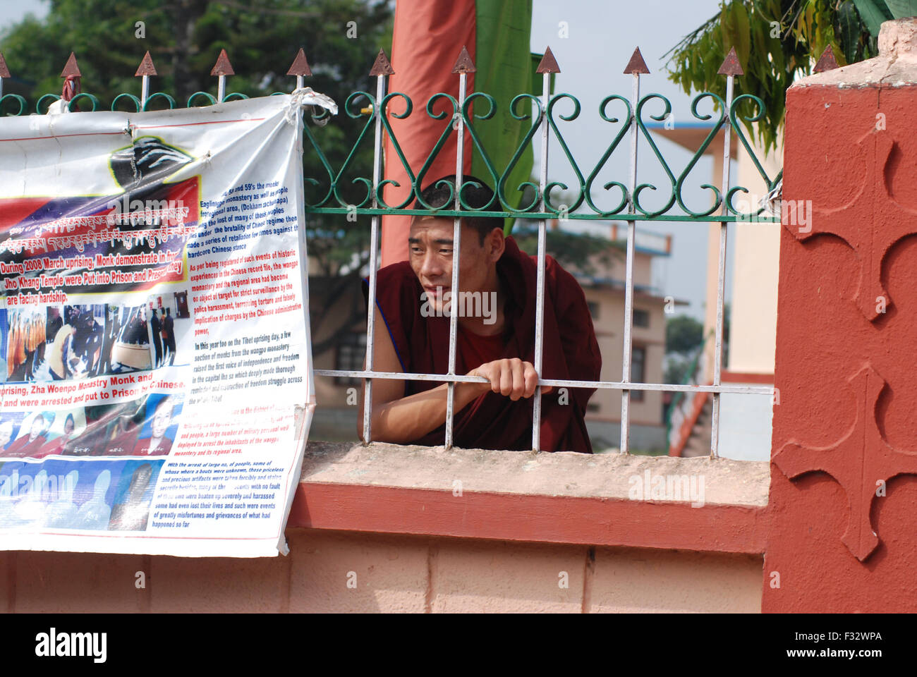 Ein Mönch späht durch einen Zaun klösterliche Universität Sera Jey.  Das Plakat neben ihm zeigt Mönche, die inhaftiert wurden. Stockfoto
