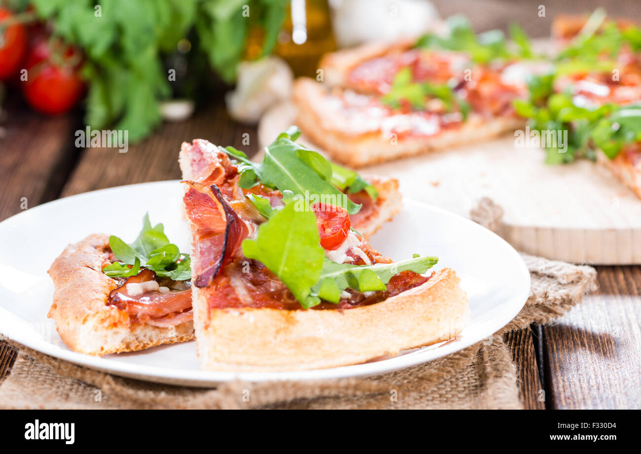 Schinken-Pizza mit Rucola und frischen Tomaten auf rustikalen hölzernen Hintergrund Stockfoto