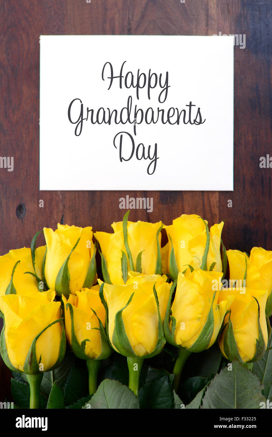 Gelbe Rosen Geschenk für Großeltern-Tag mit Grußkarte auf dunklen Vintage Holz Tisch. Stockfoto