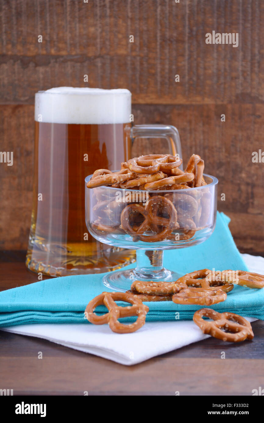 Glas Bier in Stein mit Mini Brezeln auf blass blauen Serviette auf Holz Hintergrund. Stockfoto