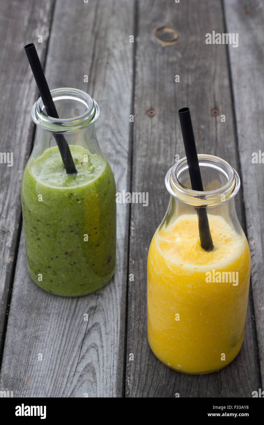 Kiwi und Orange Saft in Glasflaschen auf graues Holz beplankt. Stockfoto