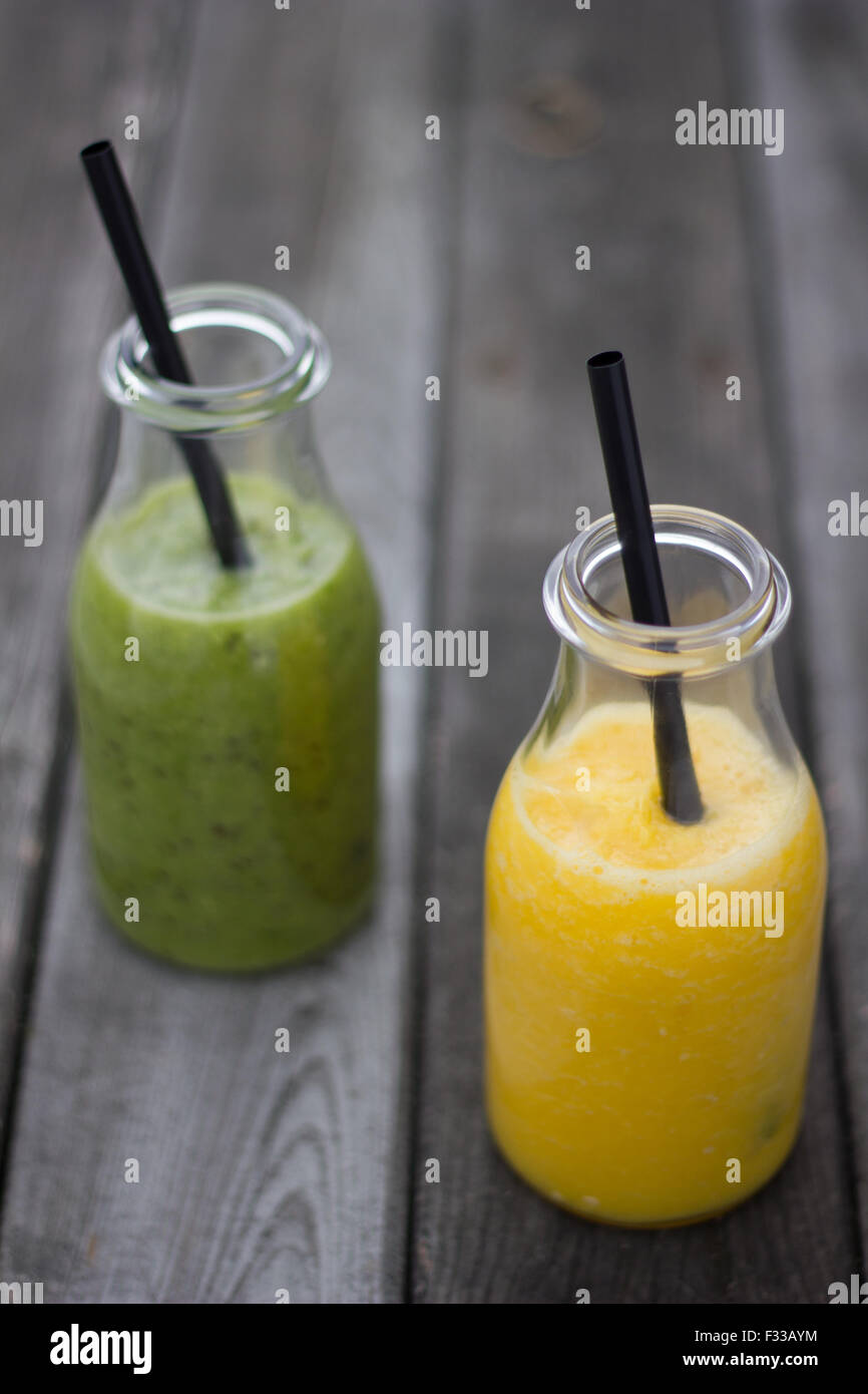 Kiwi und Orange Saft in Glasflaschen auf graues Holz beplankt. Stockfoto