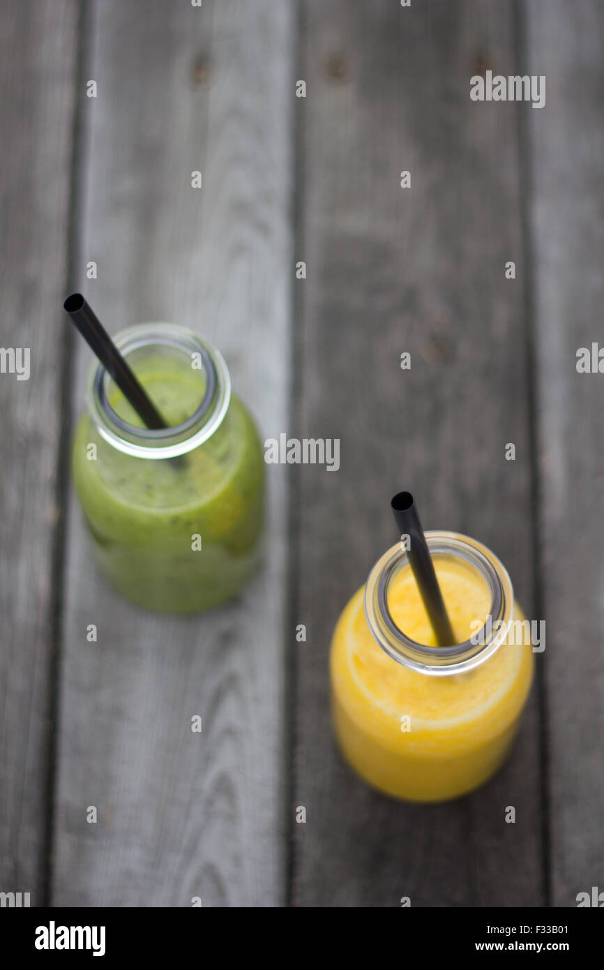 Kiwi und Orange Saft in Glasflaschen auf graues Holz beplankt. Stockfoto