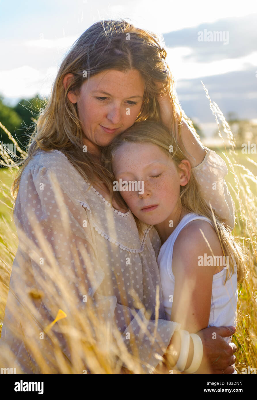 Eine Hintergrundbeleuchtung Porträt einer Frau (Alter 25-30) mit ihrer Tochter (8 Jahre) saß in einem Feld lange Gras auf einen Sommerabend Stockfoto