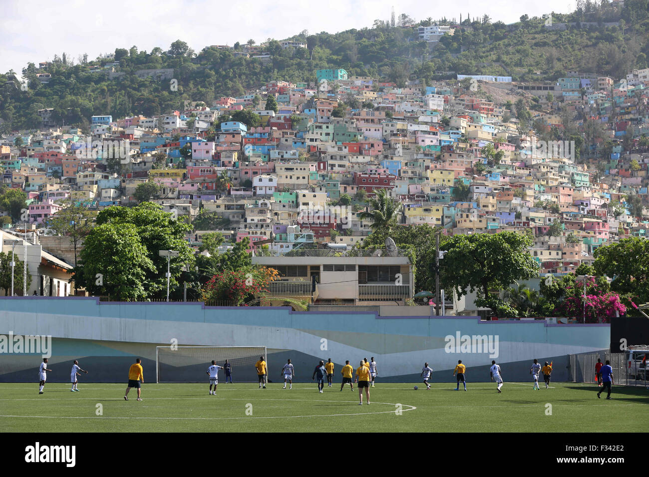 Erwachsene spielen Fußball auf dem Fußballplatz Park Sainte Thérèse mit bunten Häusern entlang der Hügel 15. September 2015 in Port-au-Prince, Haiti. Stockfoto
