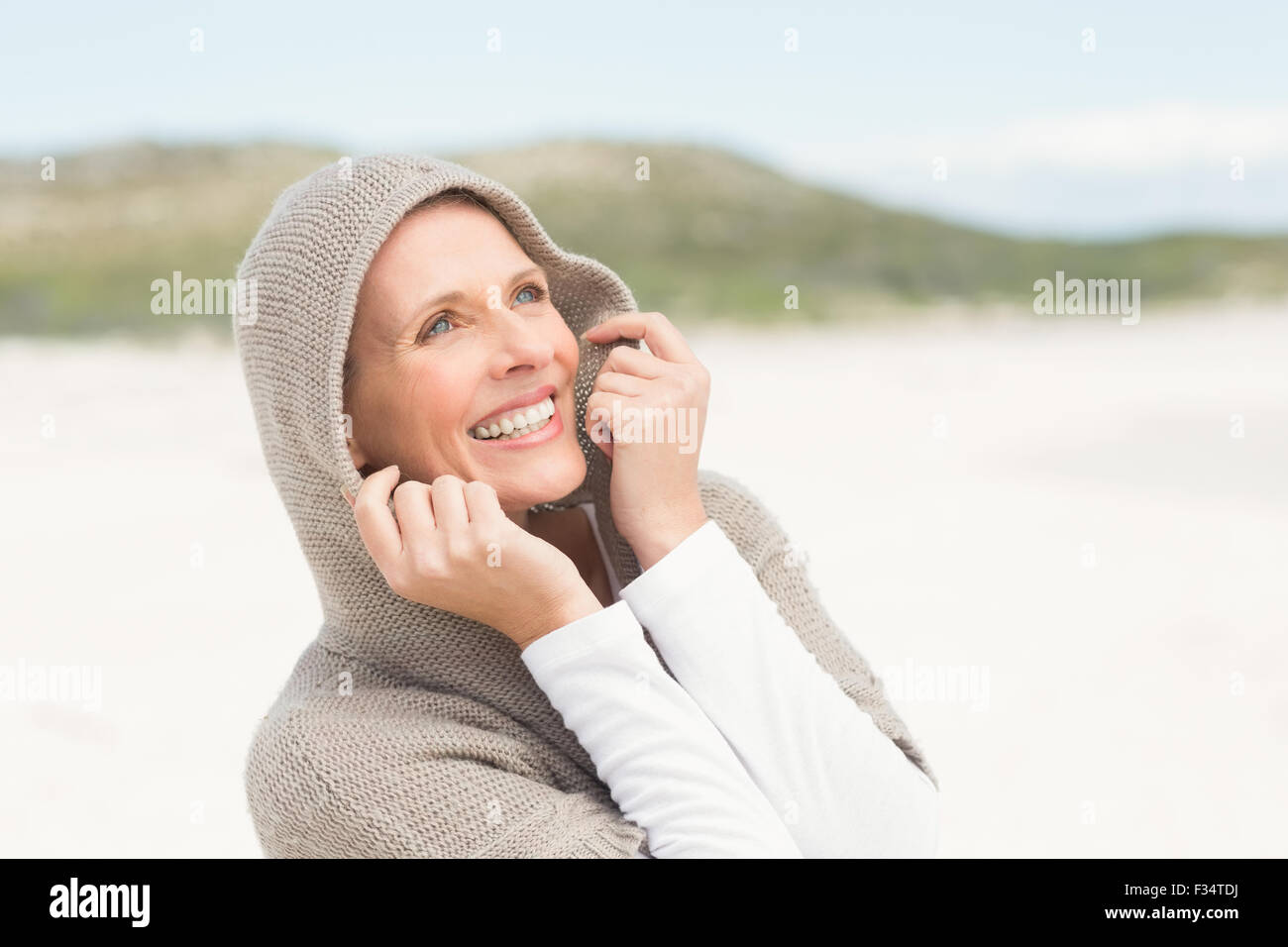 Lächelnde Frau aufstehen auf dem Sand mit Kapuze Stockfoto