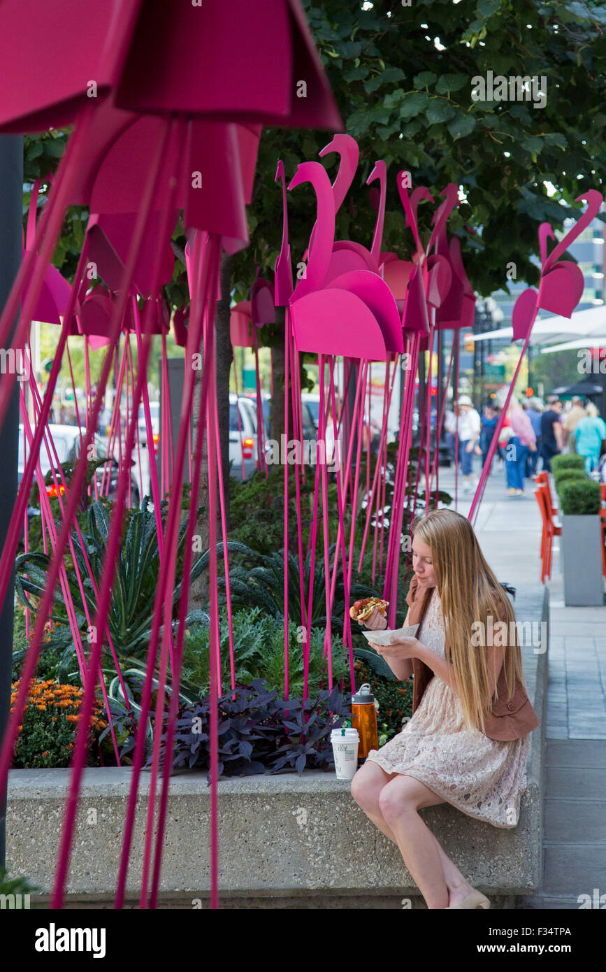 Grand Rapids, Michigan - eine Frau isst Mittagessen auf der Straße unter einem Wald von rosa Flamingos während des jährlichen ArtPrize-Festival. Stockfoto