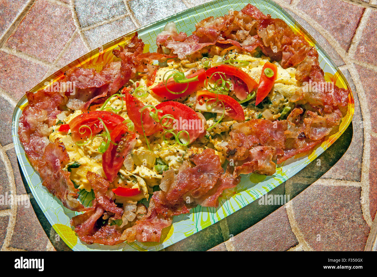 Eine Frühstück-Ei-Omelette mit Käse, Zwiebeln, Paprika, Frühlingszwiebeln Streifen, Tomaten Keile und fettig, gebratenen Speck. Stockfoto