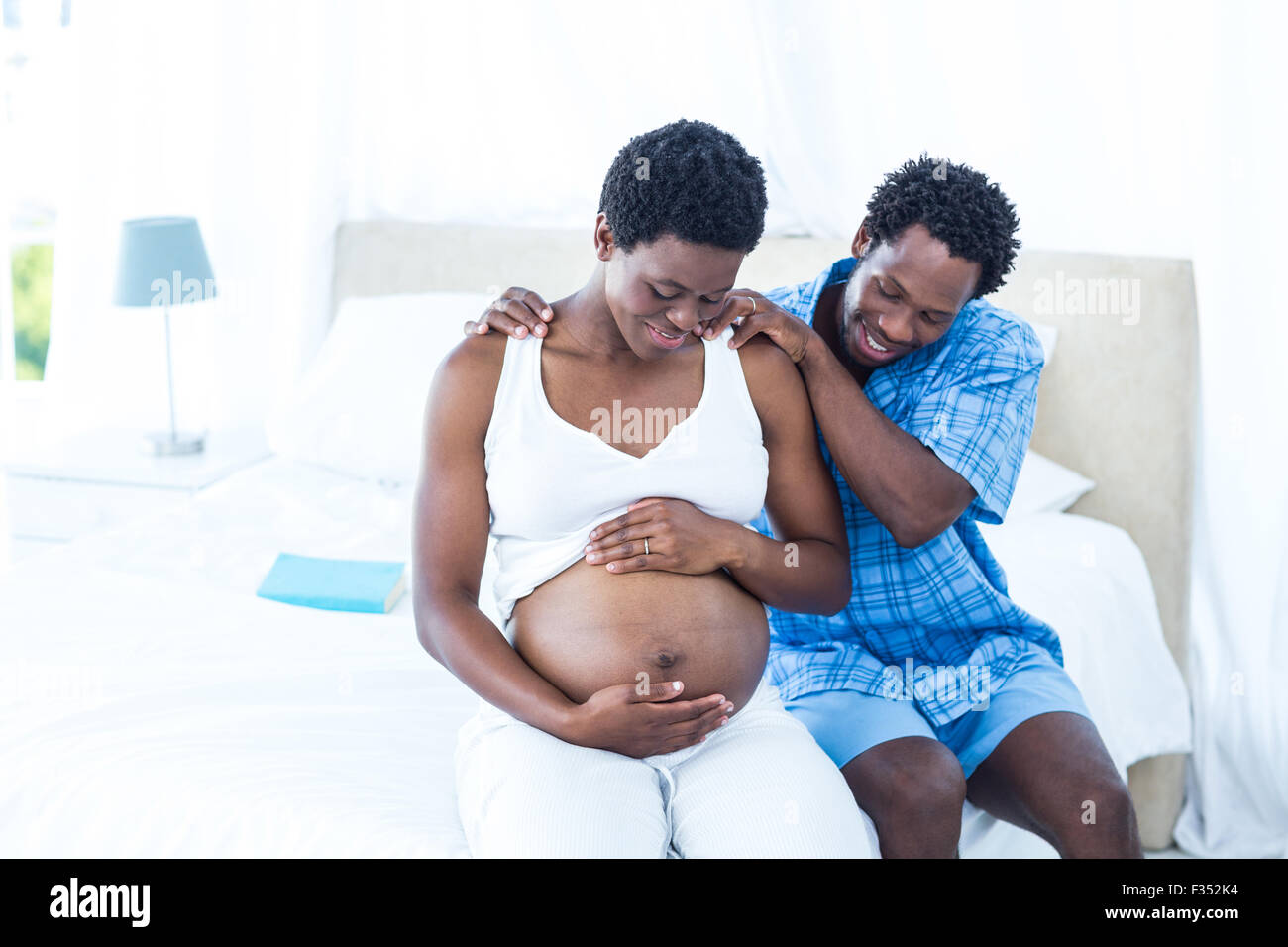 Mann massiert schwangere Frau auf dem Bett sitzend Stockfoto
