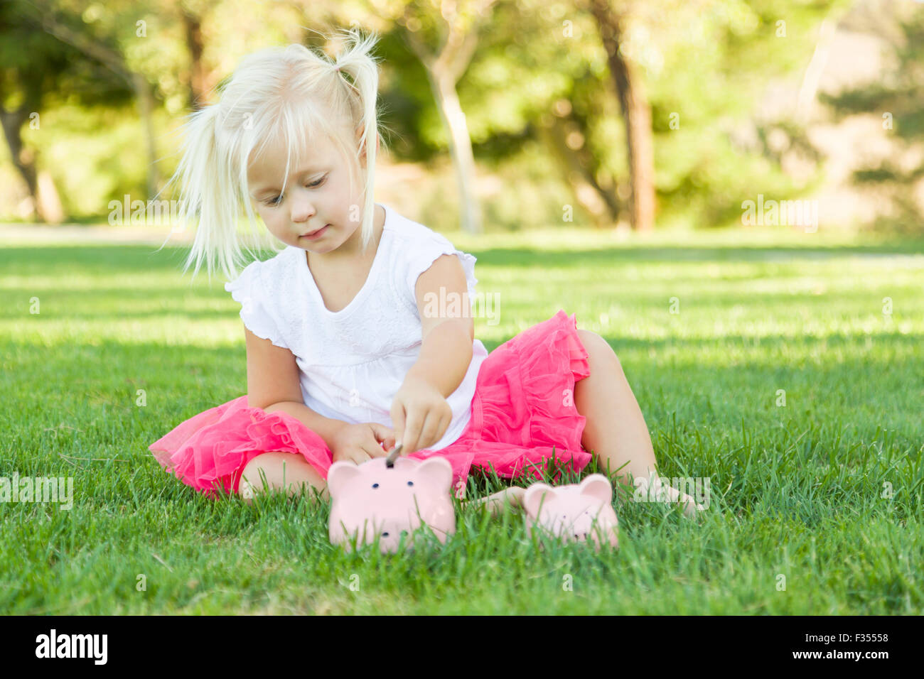 Niedliche kleine Mädchen Spaß mit ihren großen und kleinen Sparschweine außerhalb auf dem Rasen. Stockfoto