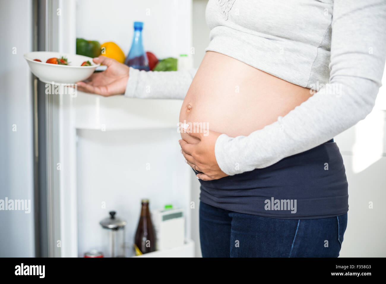 Schwangere Frau Erdbeeren im Kühlschrank zu halten, während der Bauch zu berühren Stockfoto