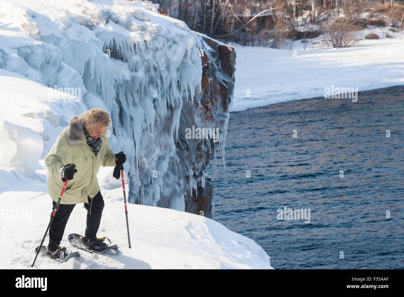 Ältere Frau mit Schneeschuhen bewegt sich über eine verschneite Bank hoch über Lake Superior im Winter, Tettegoche, MN, USA Stockfoto