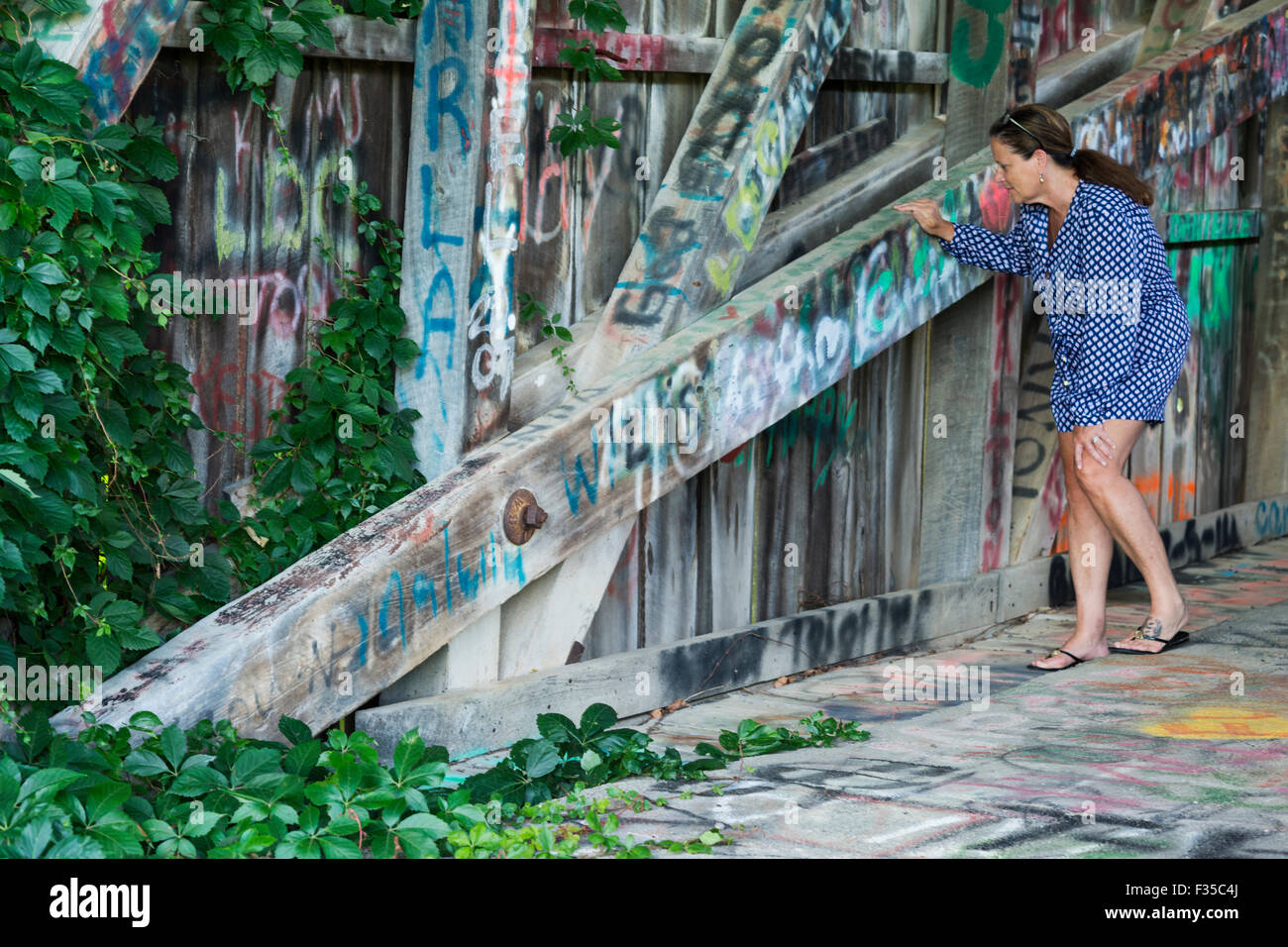 Frau in 50er Jahren schaut an Graffiti auf den Holzbalken eine überdachte Brücke, KY, USA Stockfoto