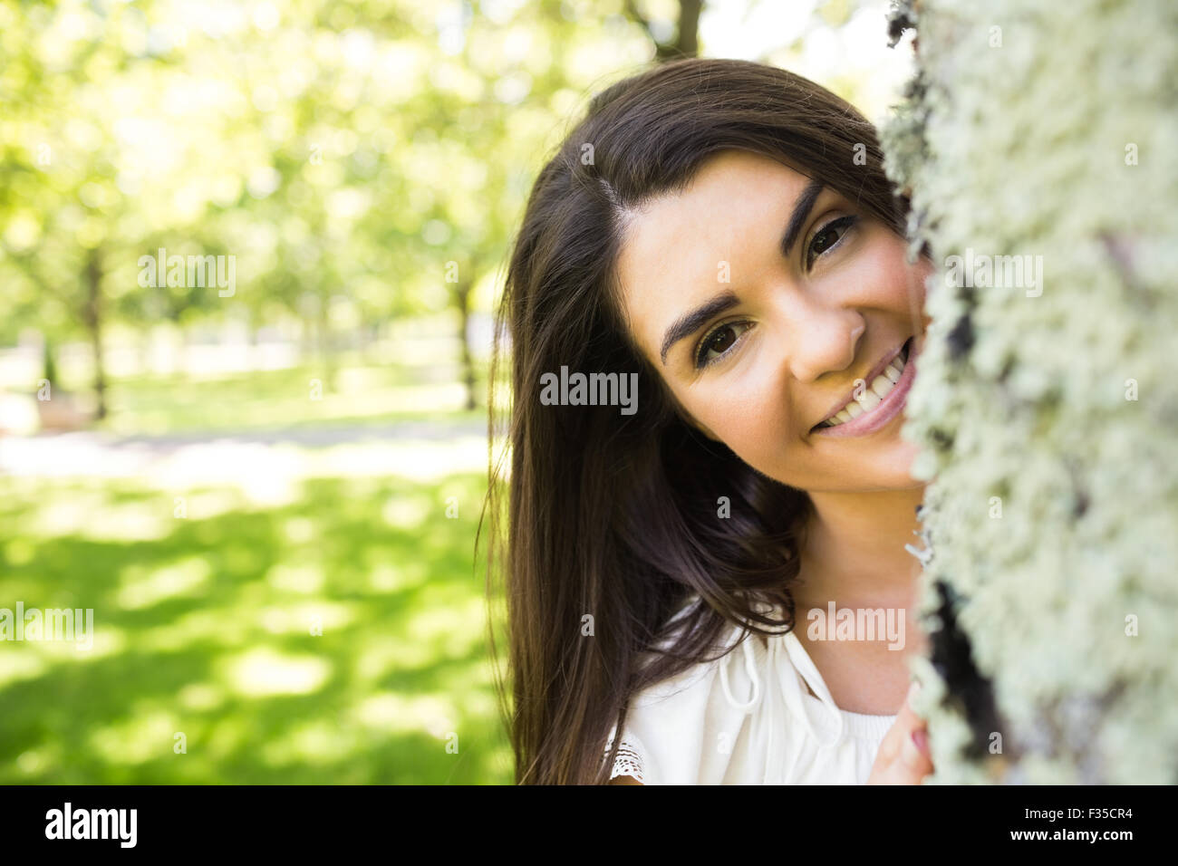 Porträt der lächelnde Frau hinter Baumstamm Stockfoto