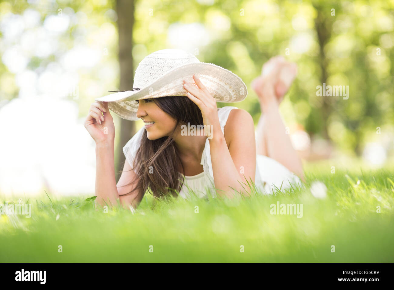 Glückliche junge Frau mit Sonnenhut liegend auf Grünland Stockfoto