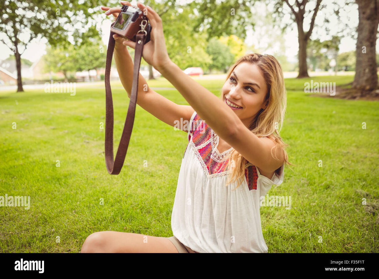 Lächelnde Frau unter Selbstporträt mit Kamera beim Sitzen auf dem Rasen Stockfoto