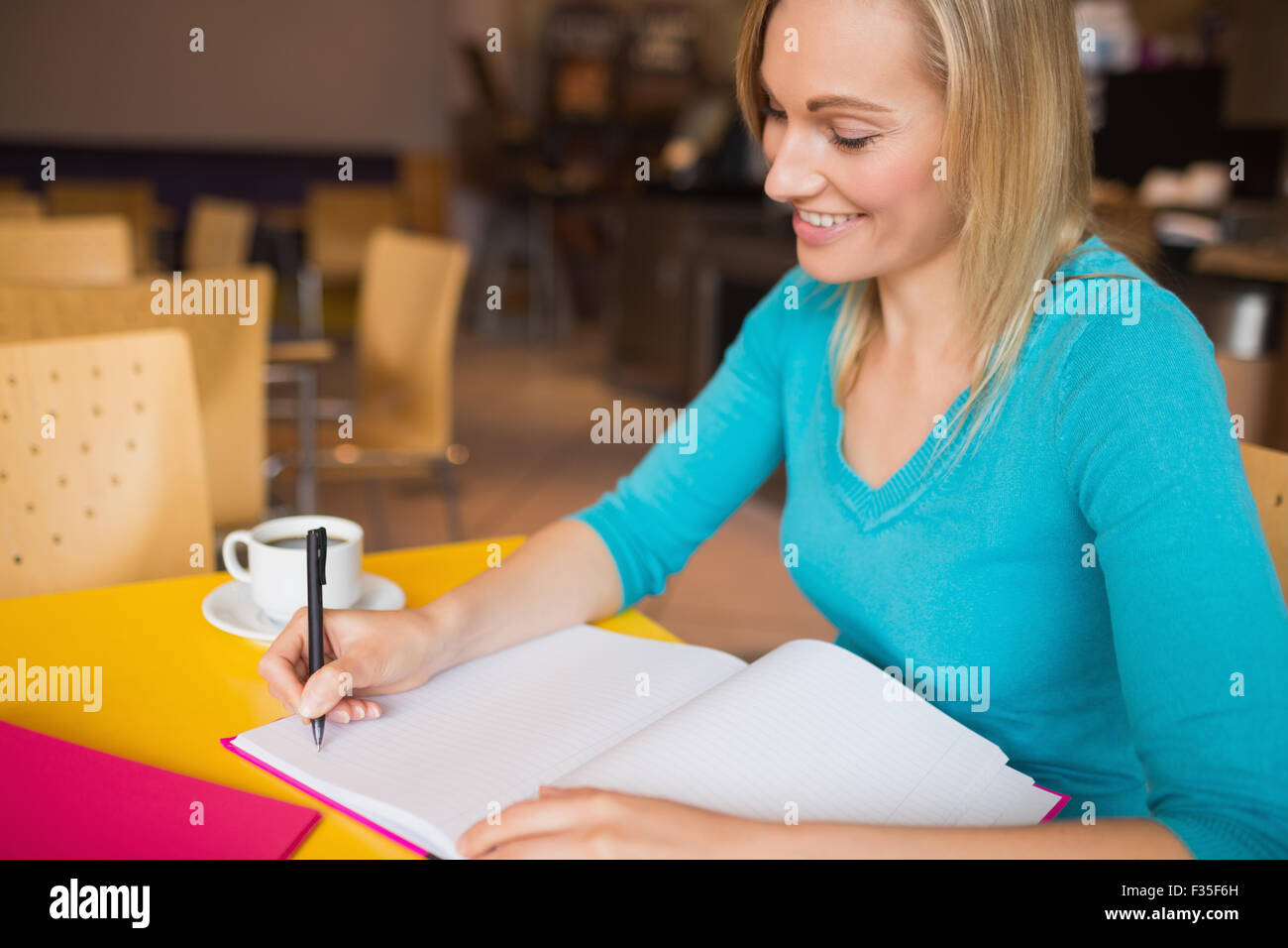 Junge Frau lächelt während des Schreibens auf Buch Stockfoto