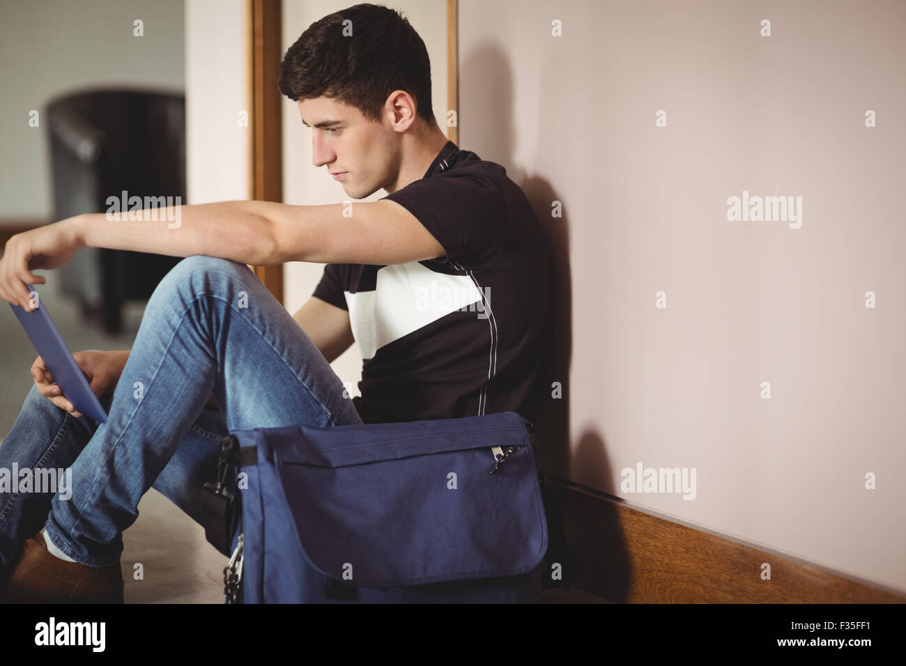 Männliche Schüler mit digital-Tablette durch die Wand in der Schule sitzen Stockfoto