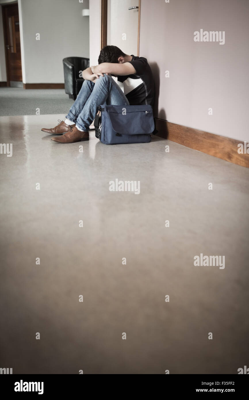 Männliche Schüler mit Kopf auf Knien sitzen durch die Wand Stockfoto