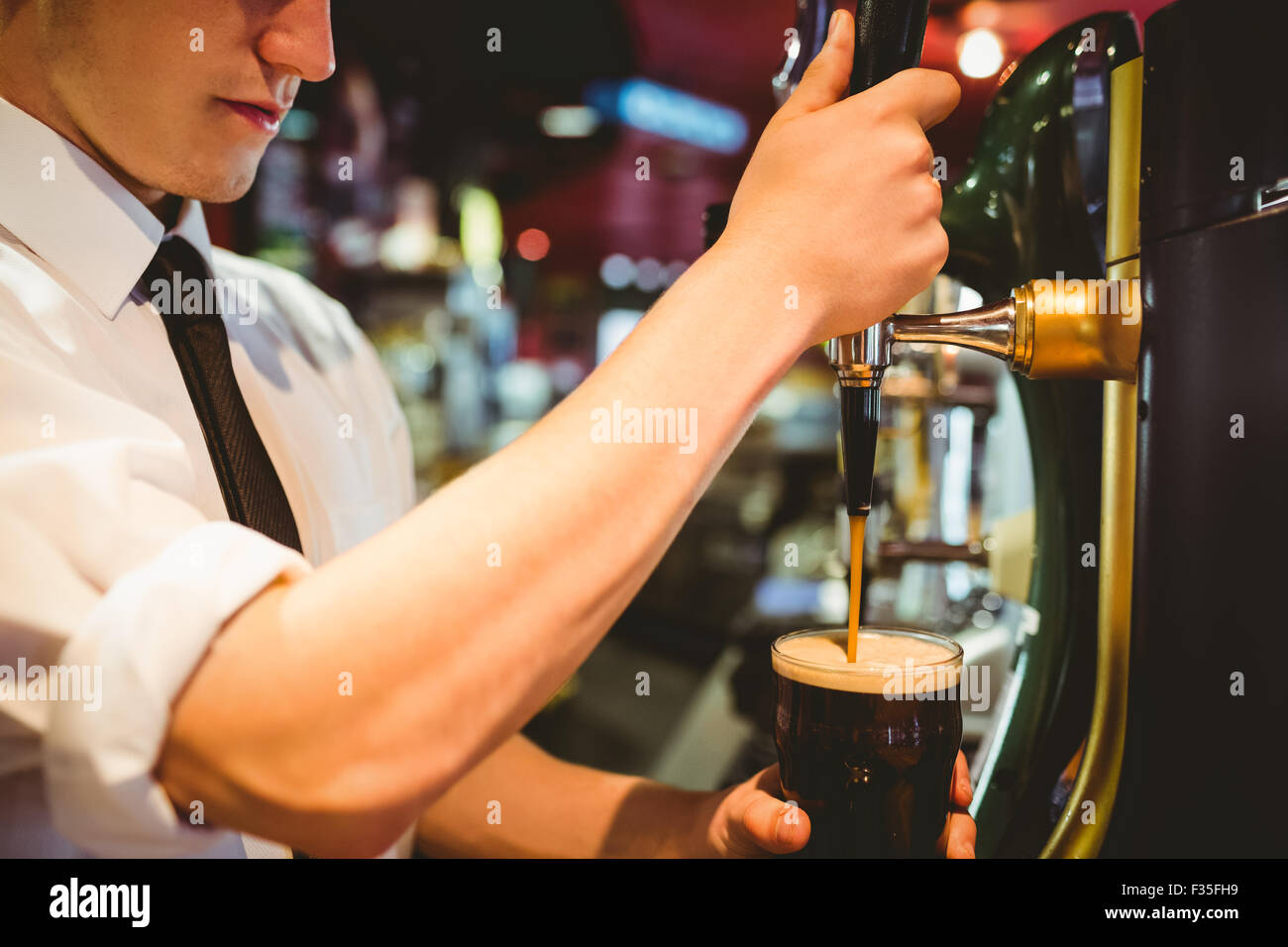 Barkeeper hält Bierglas unter Dispenser Hahn Stockfoto