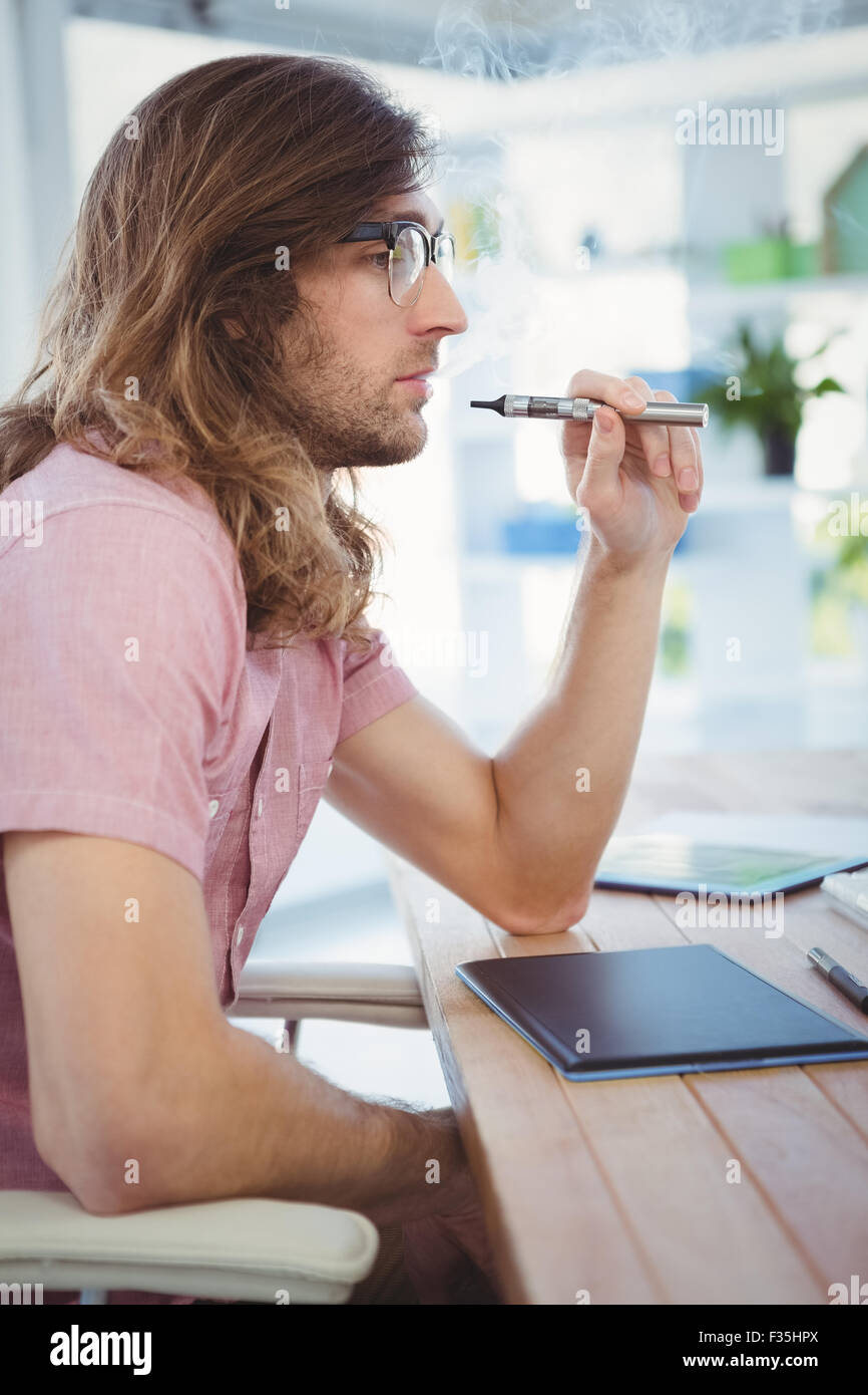 Hipster rauchen elektronische Zigarette am Schreibtisch im Büro Stockfoto