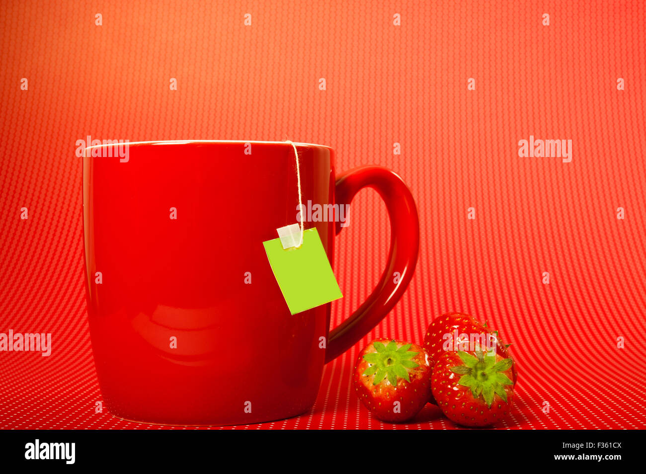 Rote Tasse mit Teebeutel und Erdbeeren, auf rotem Grund Stockfoto