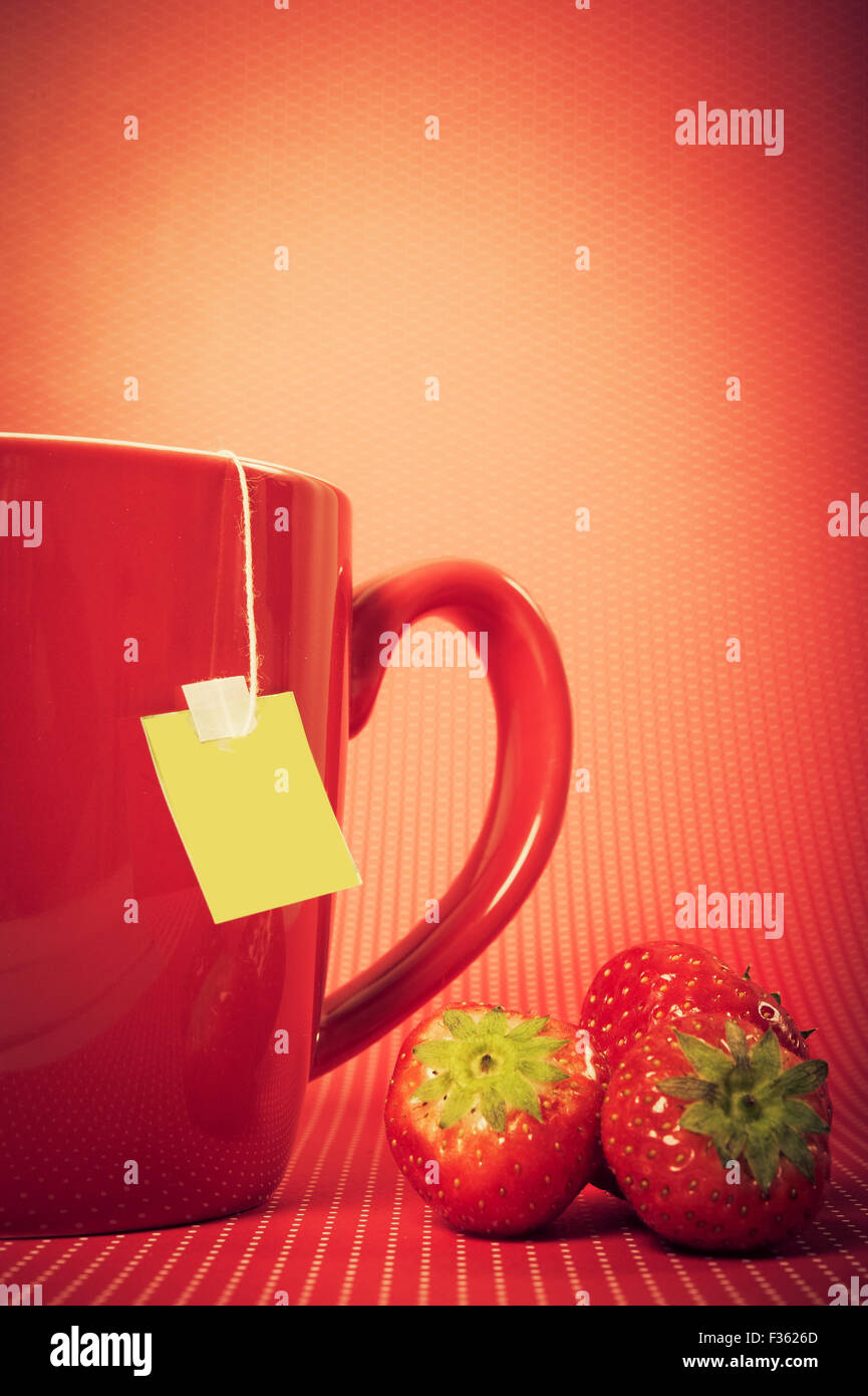 Rote Tasse mit Teebeutel und Erdbeeren, auf rotem Grund Stockfoto