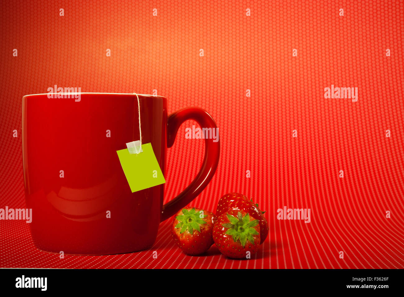 Rote Tasse mit Teebeutel und Erdbeeren, auf rotem Grund Stockfoto
