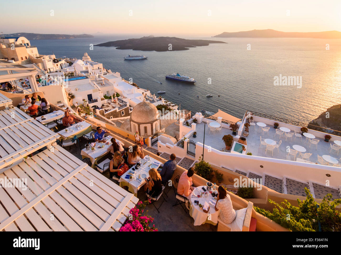 Restaurants mit Blick auf die Caldera und Nea Kameni von Fira bei Sonnenuntergang auf Santorin, Kykladen, Griechenland Stockfoto