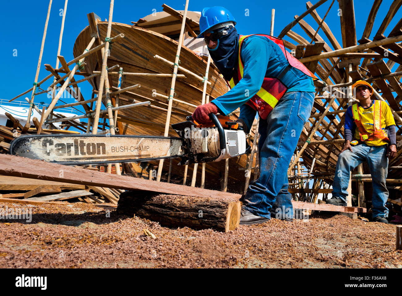 Ein Schiffsbauer schneidet ein Brett mit einer Kettensäge beim Bau eines traditionellen hölzernen Fischereifahrzeug in einer Werft in Manta, Ecuador. Stockfoto