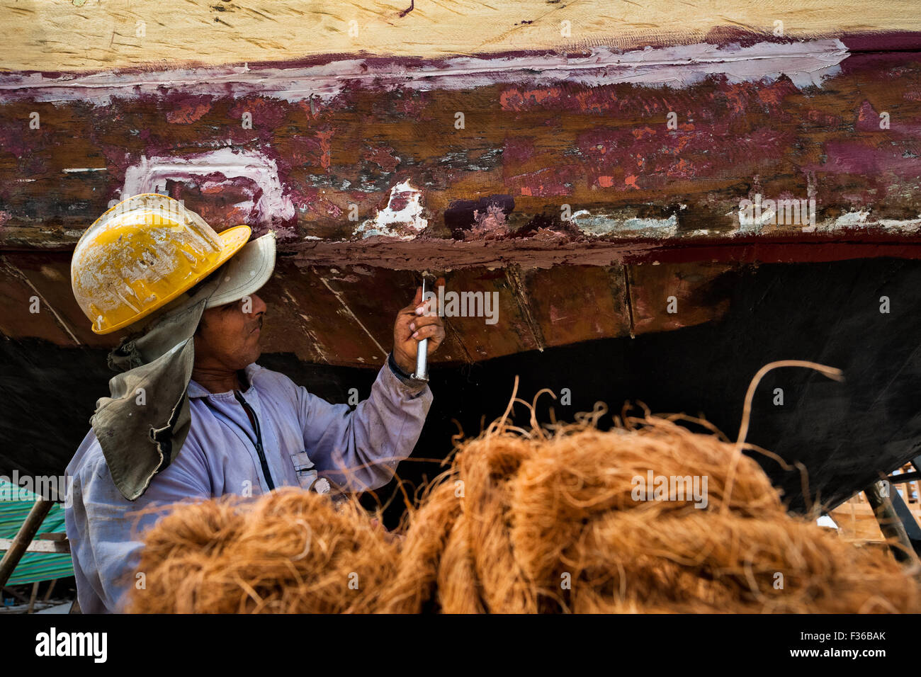 Ein ecuadorianischer Arbeiter caulks eines traditionellen hölzernen Fischereifahrzeug in einer Werft in Manta, Ecuador. Stockfoto