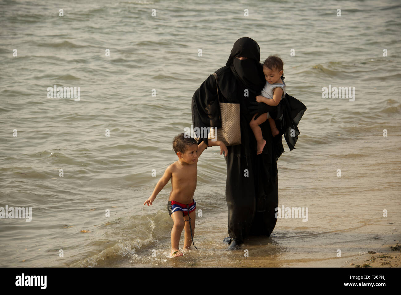 Muslimische Mutter und ihren beiden Kindern zu Fuß in das Rote Meer von der Corniche in Jeddah, Saudi Arabien Stockfoto