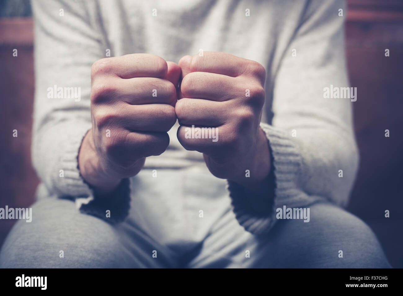 Junger Mann sitzt auf einem Sofa mit seiner geballten Fäusten Stockfoto