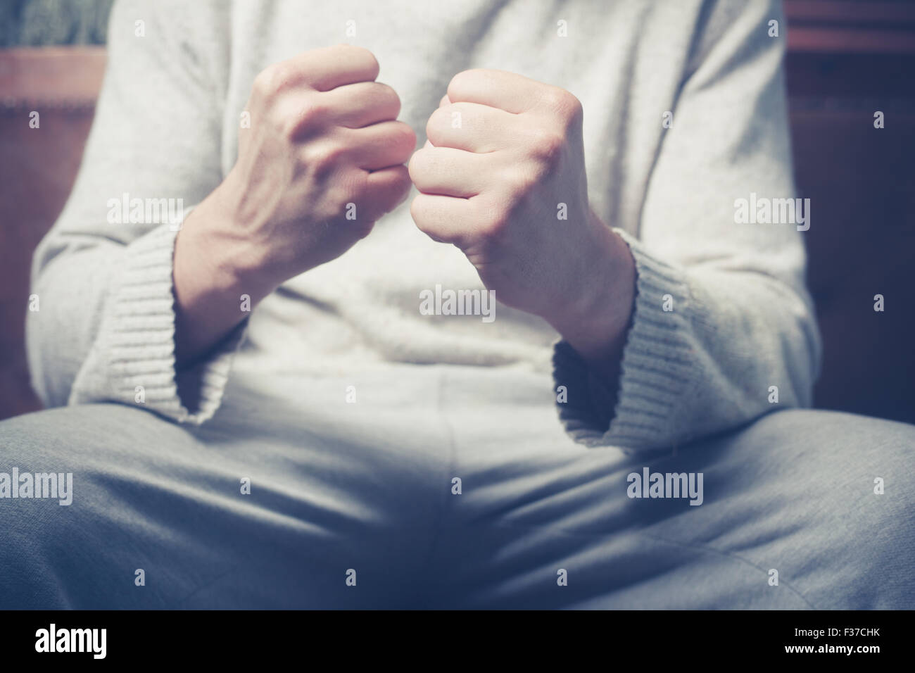 Junger Mann sitzt auf einem Sofa mit seiner geballten Fäusten Stockfoto