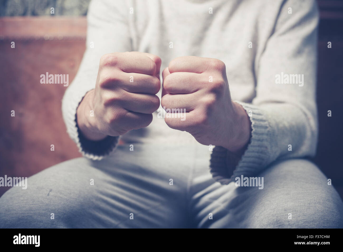 Junger Mann sitzt auf einem Sofa mit seiner geballten Fäusten Stockfoto