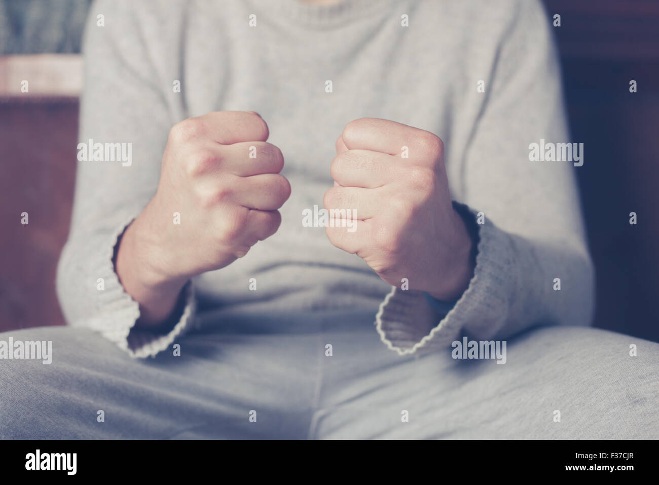 Junger Mann sitzt auf einem Sofa mit seiner geballten Fäusten Stockfoto