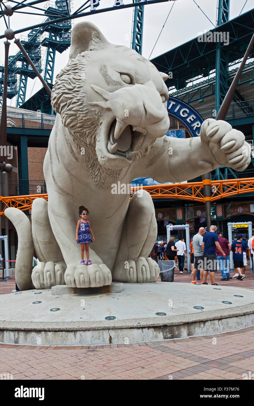 Detroit, Michigan - ein kleines Mädchen posiert für ein Bild unter einer Statue eines Tigers im Comerica Park, Heimat der Detroit Tigers. Stockfoto