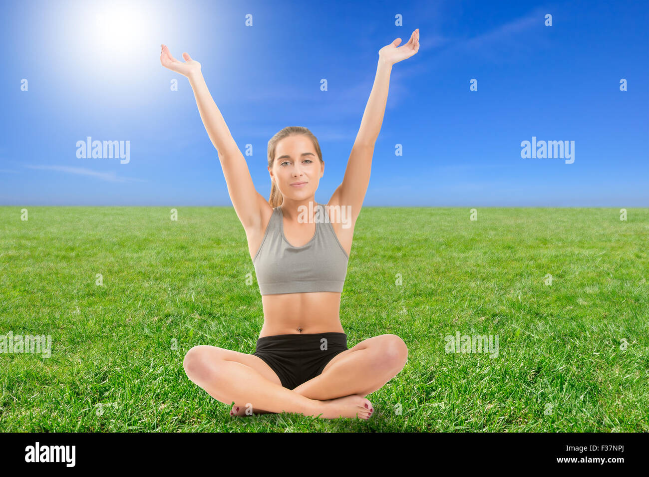 Frau praktizieren Yoga mit ihren Armen in der Luft sitzen auf dem Rasen, Hintergrundbeleuchtung Stockfoto