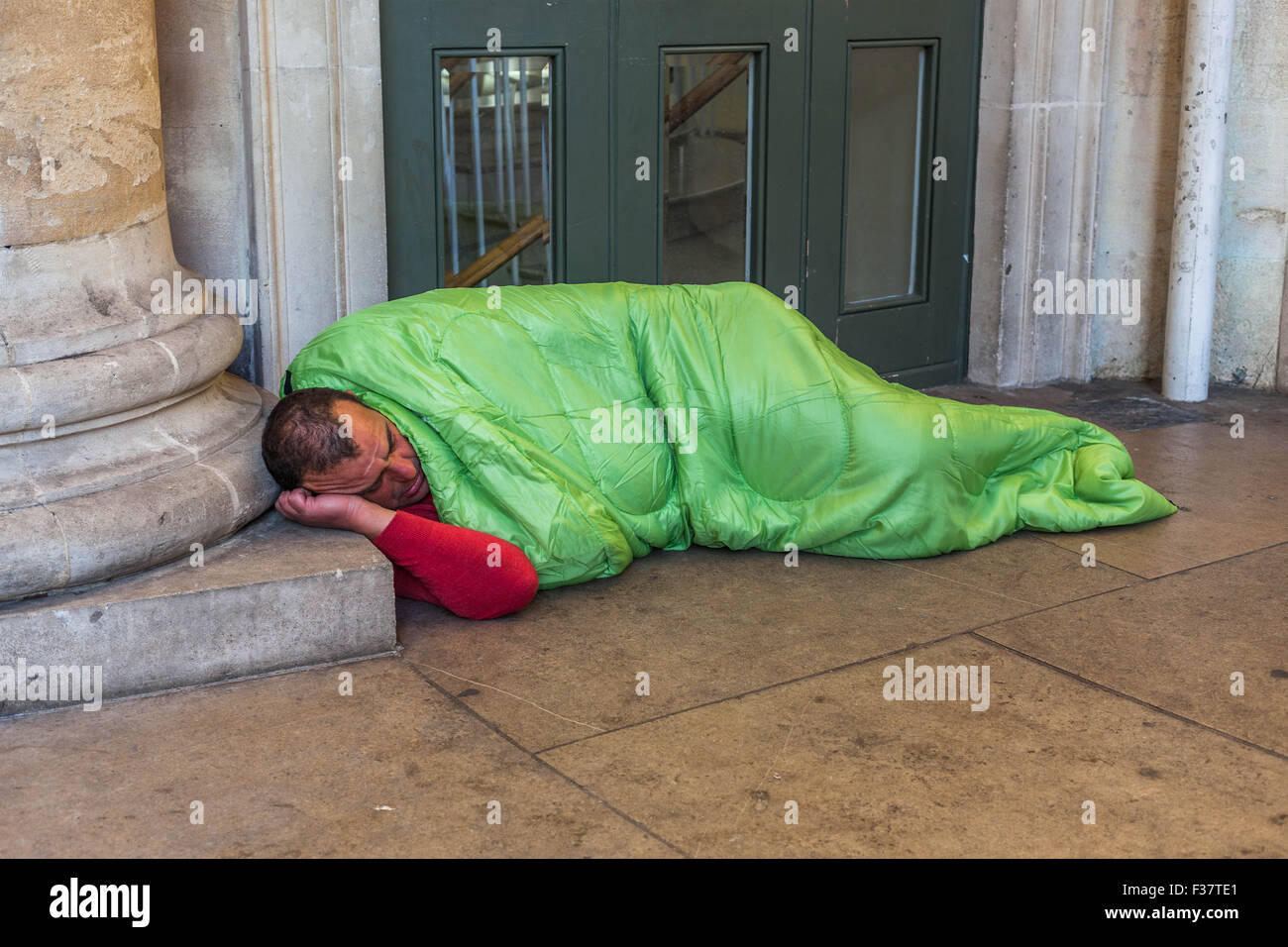 Obdachloser Mann, der an einer Tür rau schläft und einen Säulensockel als Kissen verwendet, London, England, Großbritannien. Stockfoto