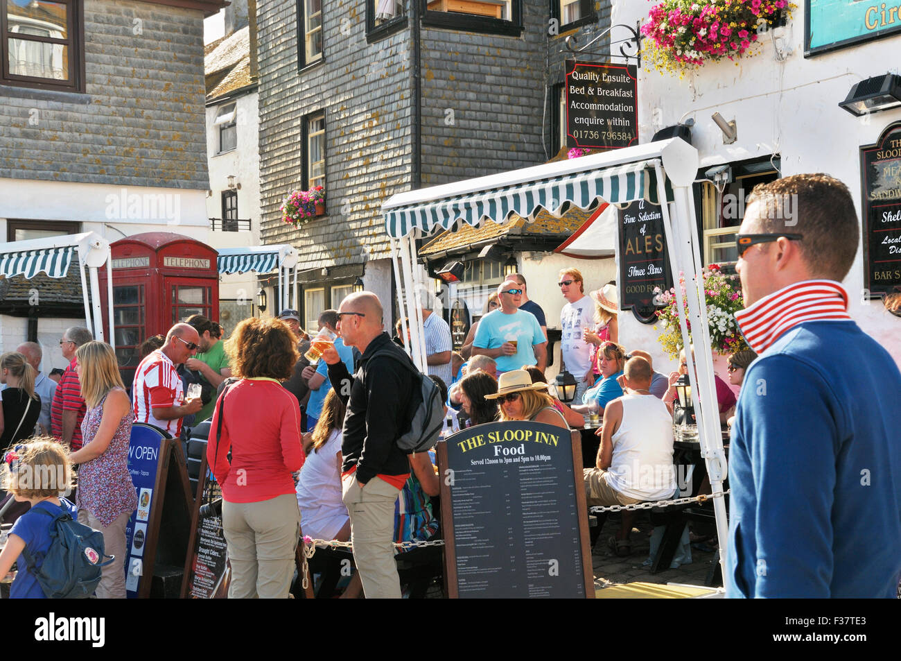 Menschen entspannen mit Getränken vor einem Pub an einem sonnigen Sommernachmittag.  Die Sloop Inn, St. Ives, Cornwall, UK Stockfoto