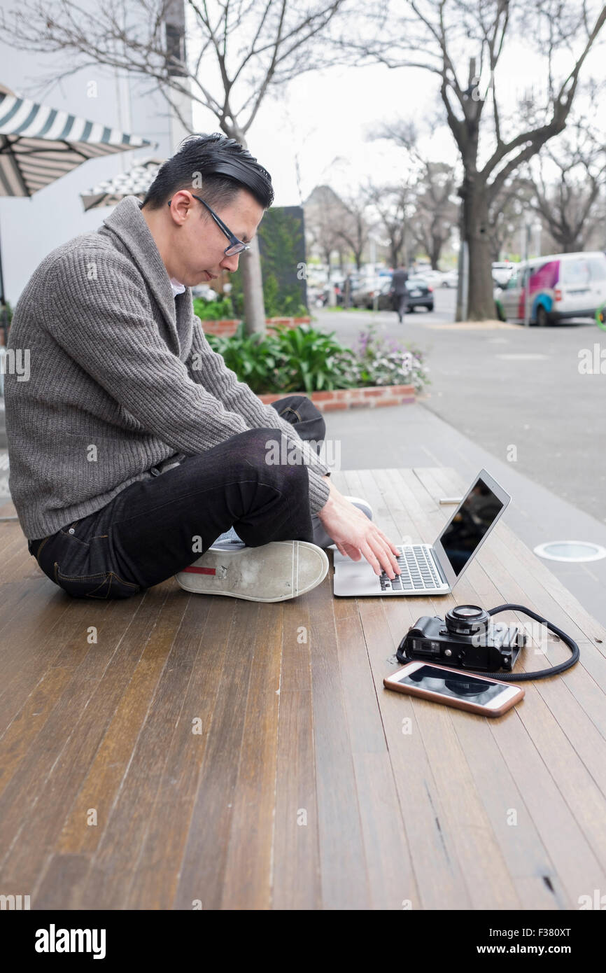 Mann am Laptop arbeiten im Freien, mit Kamera und Telefon Stockfoto
