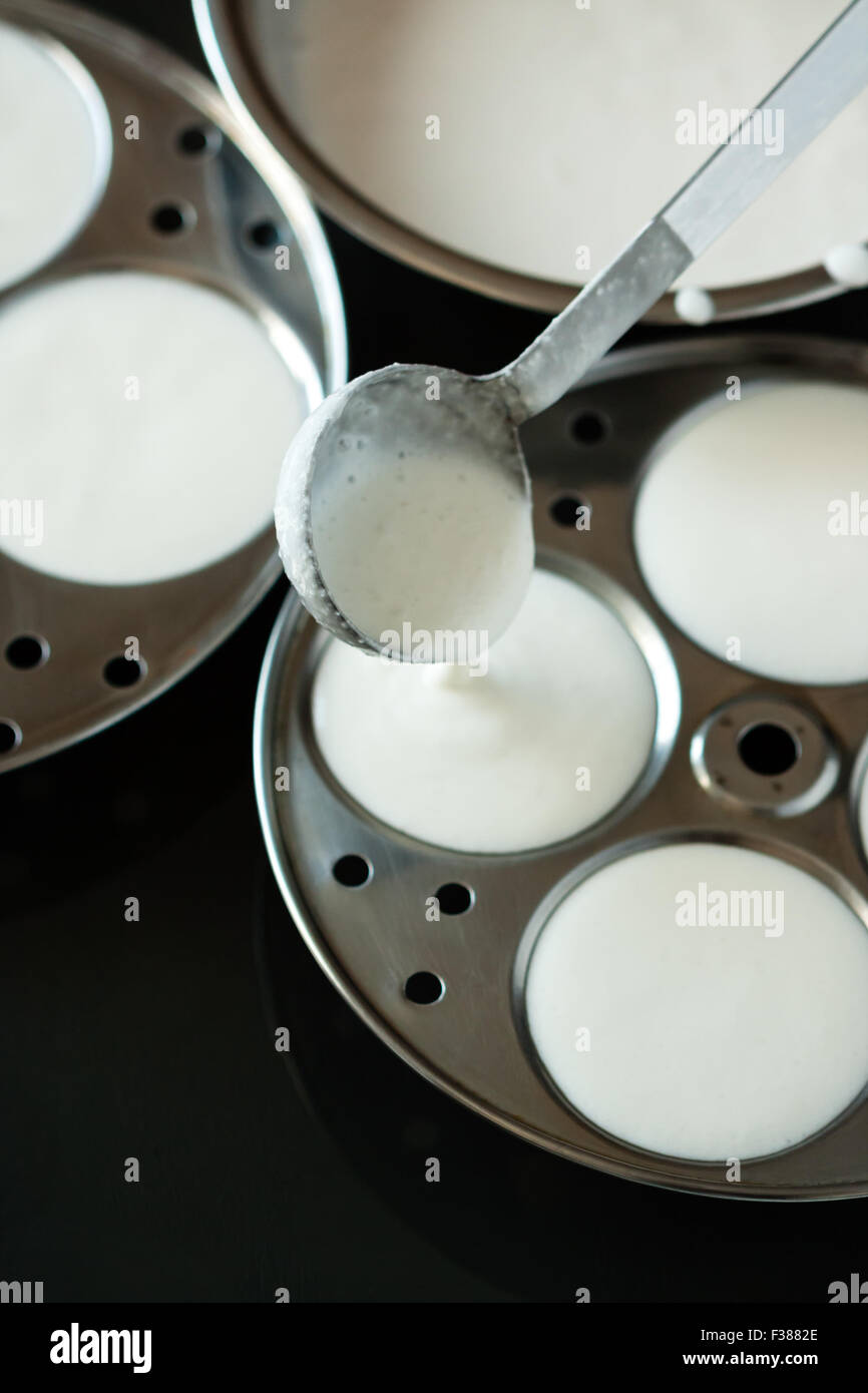Frischen Teig mit einer Kelle in kreisförmigen Trays für die Zubereitung von indischen untätig gegossen (Idli / Reis Kuchen) durch dämpfen. Stockfoto