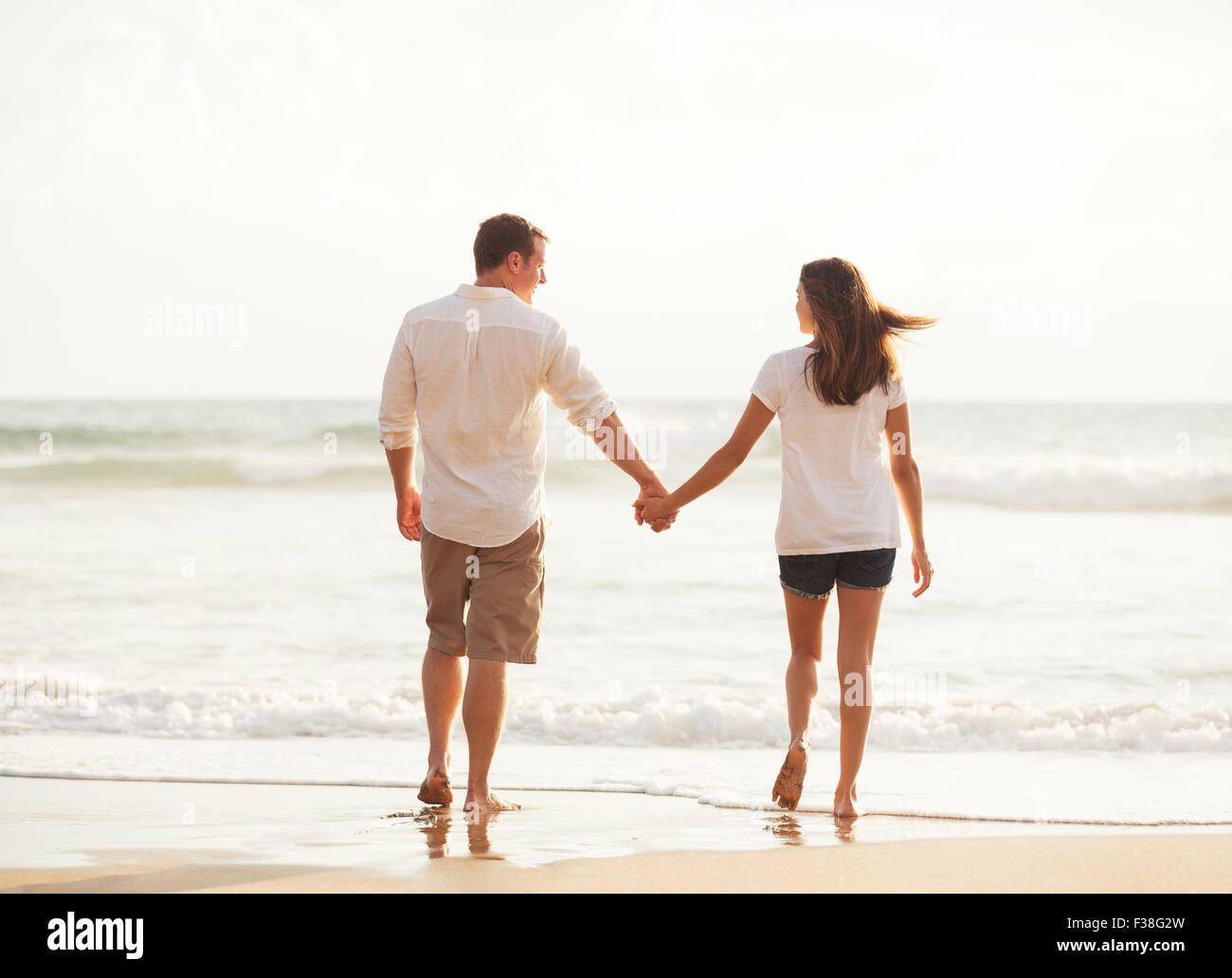 Romantische junge Brautpaar einem Strandspaziergang bei Sonnenuntergang im Urlaub Stockfoto