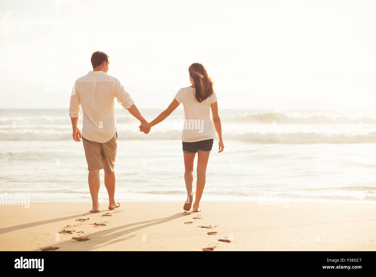 Glückliches Paar zu Fuß am Meer entlang am Strand bei Sonnenuntergang Stockfoto