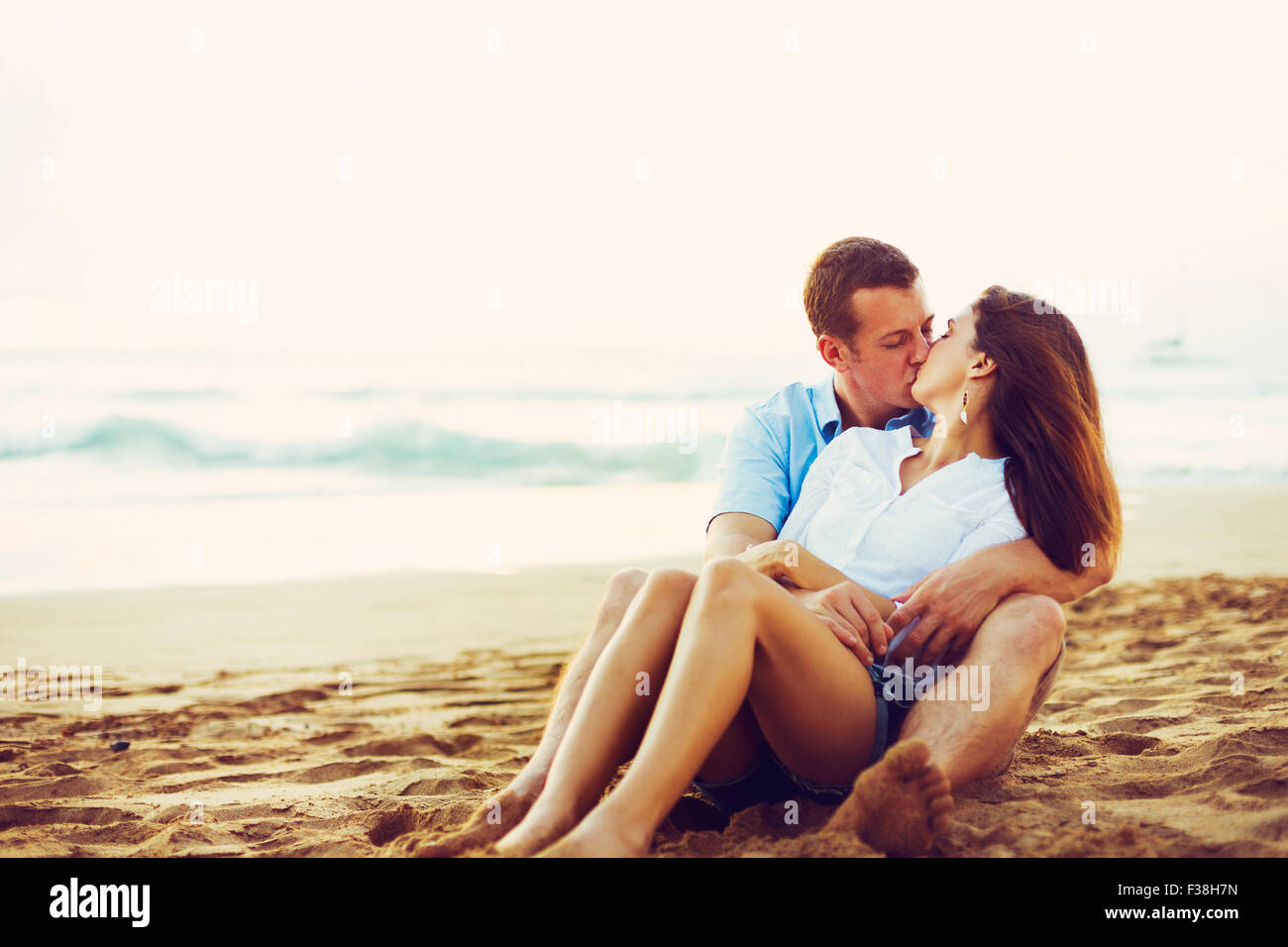 Glückliche junge romantische Paar am Strand entspannen. Küssen und den Sonnenuntergang beobachten Stockfoto