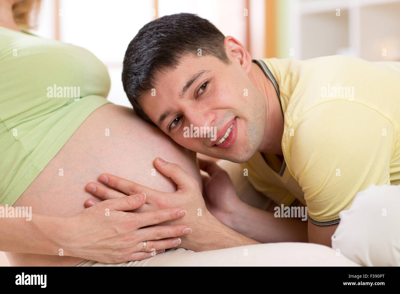 Anhören der Bauch seiner schwangeren Frau Mann Stockfoto