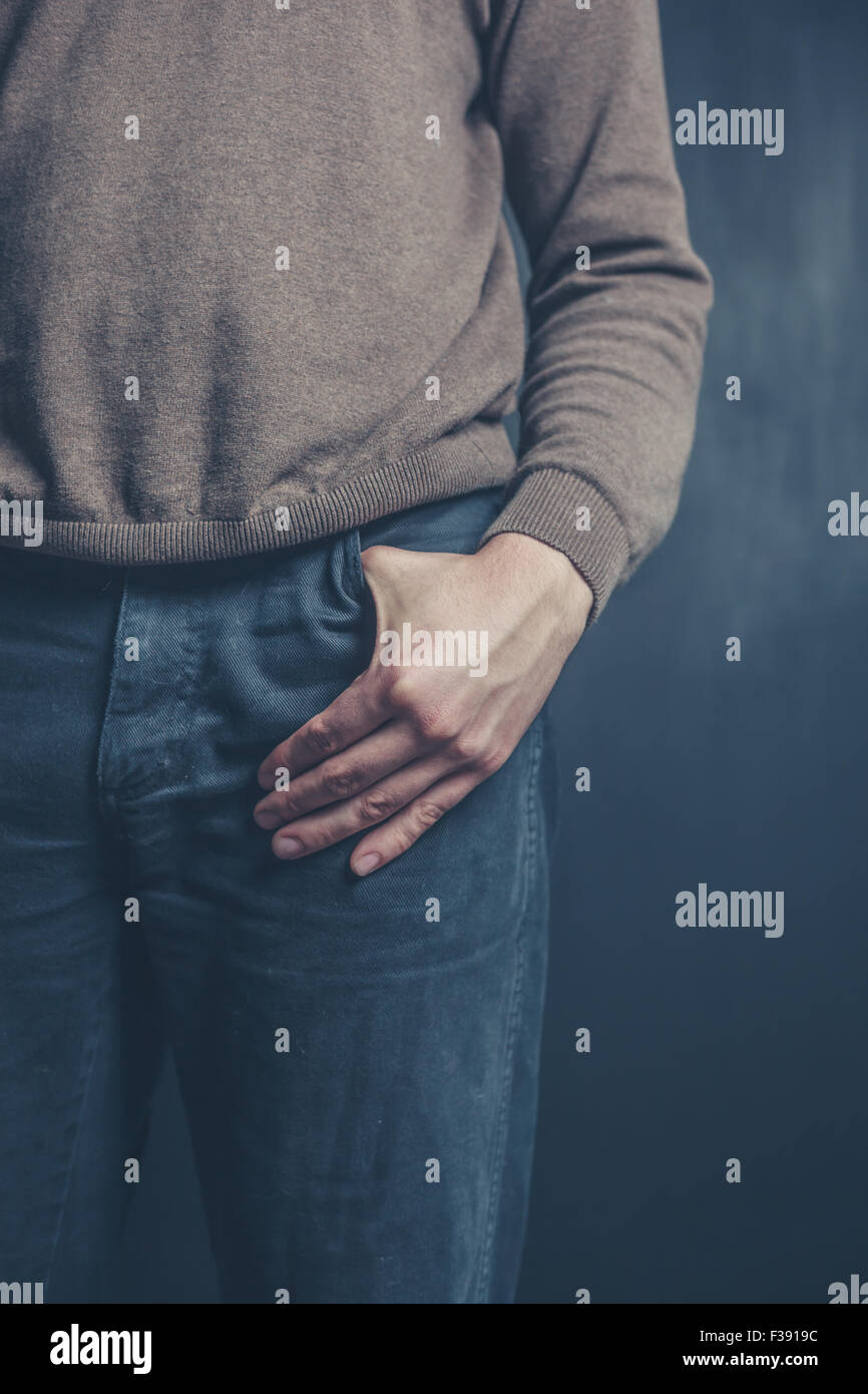 Ein junger Mann steht vor einem schwarzen Hintergrund mit seiner Hand in der Tasche Stockfoto